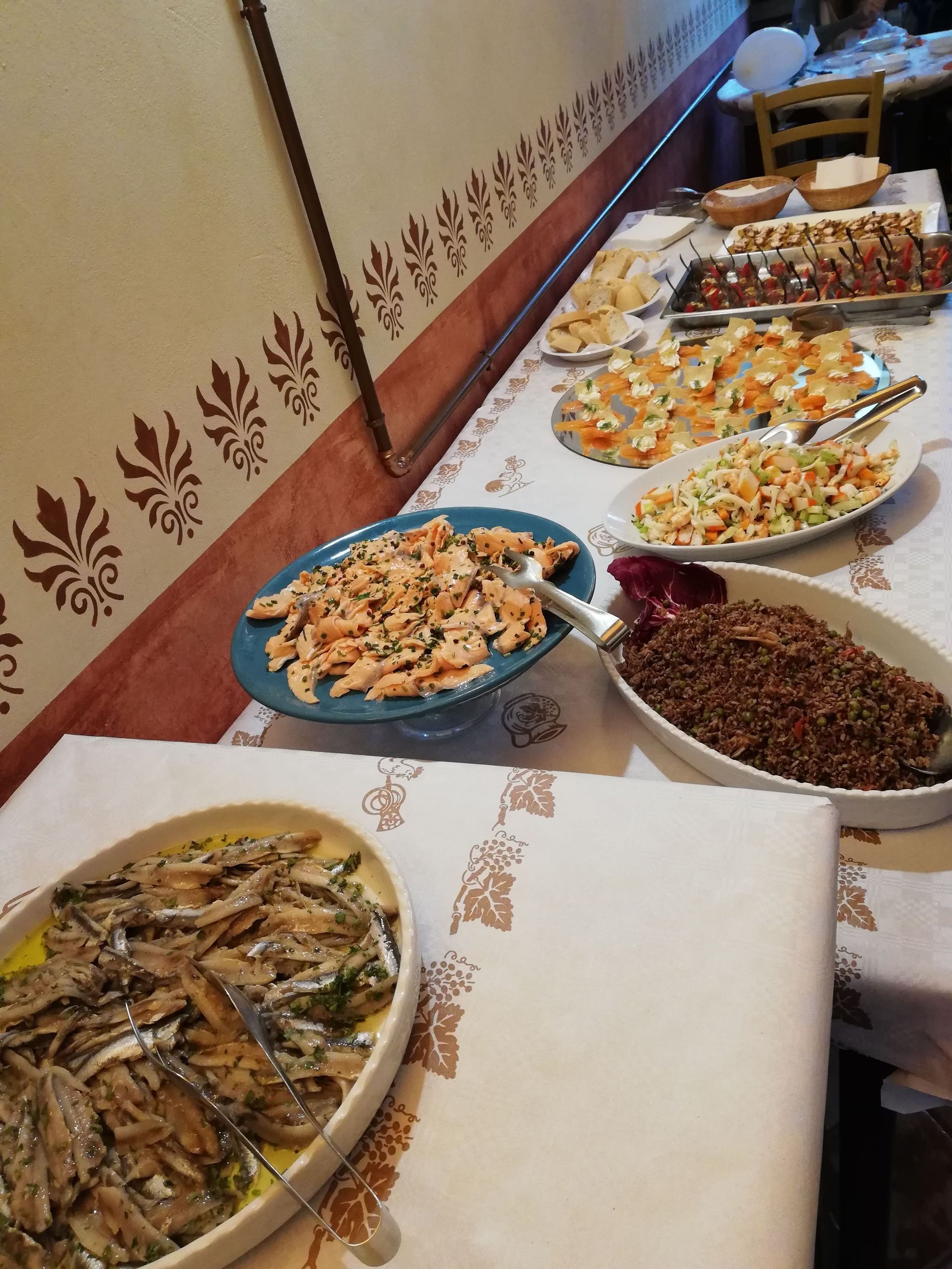 Tavolo da buffet con diversi vassoi di fritti e piatti misti su una tovaglia decorata.