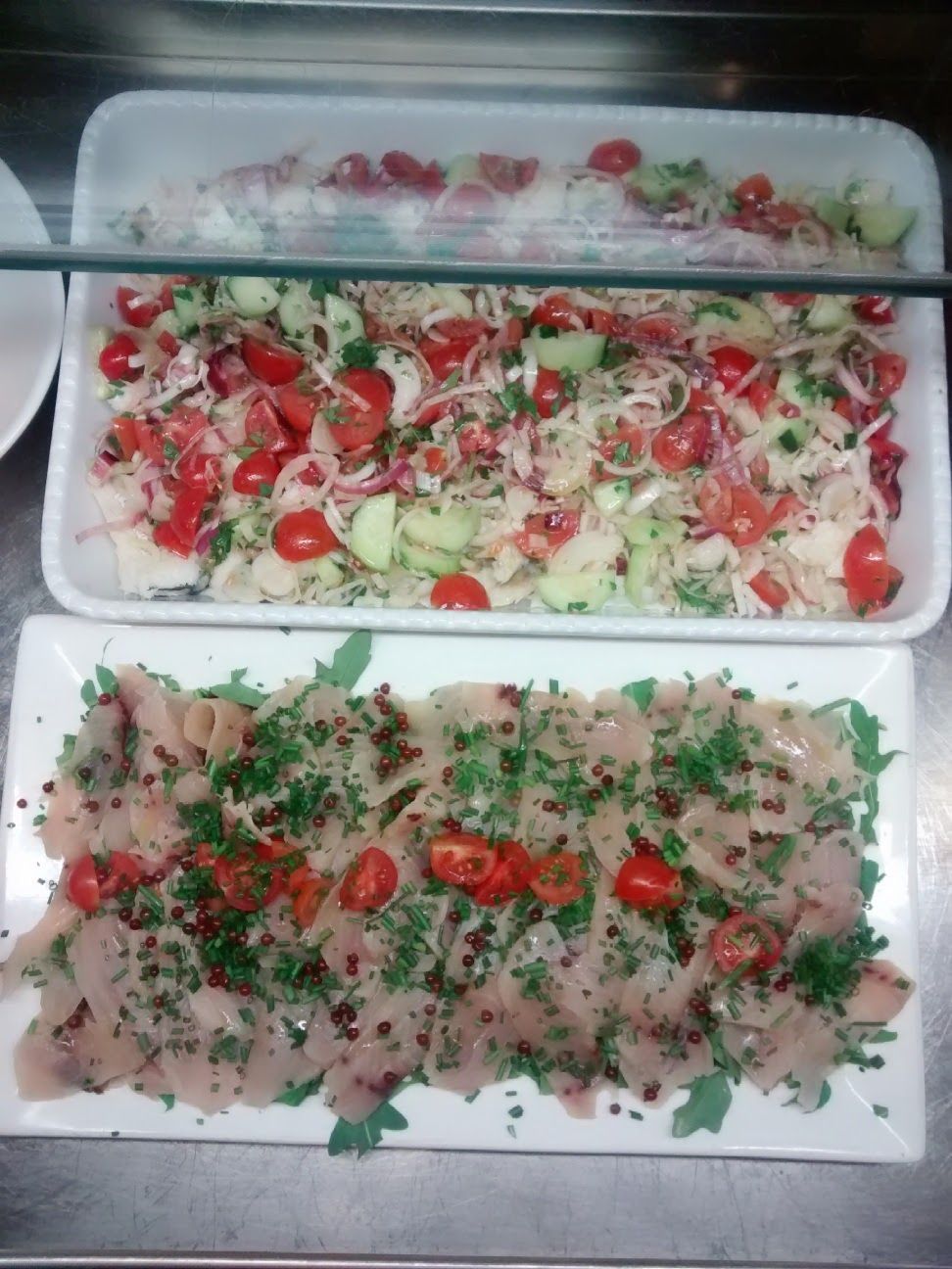 Tre vassoi di cibo affettato guarnito con pomodori ed erbe aromatiche, disposti su un tavolo.