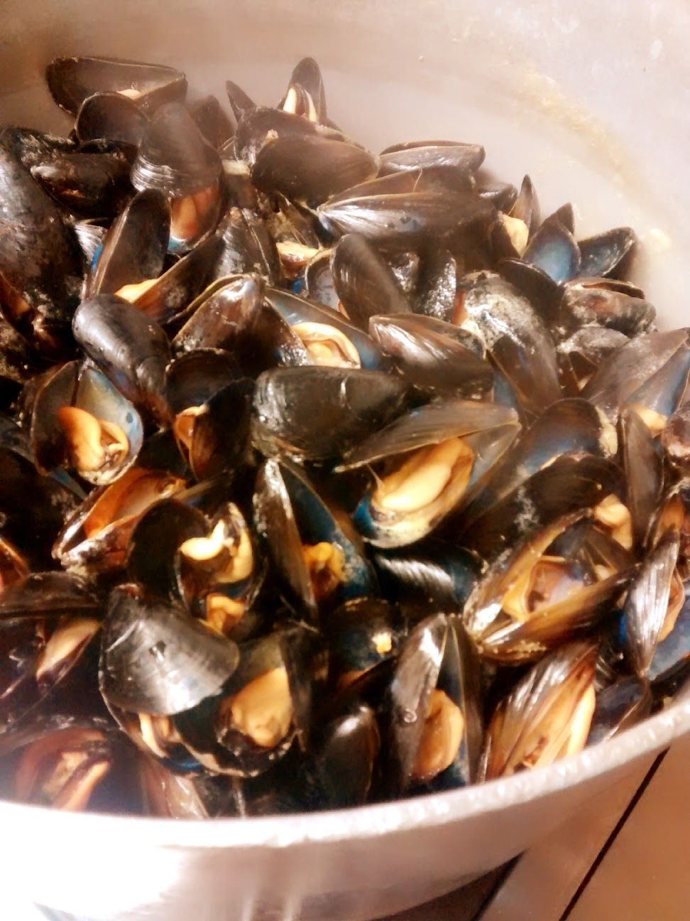 Una ciotola piena di cozze al vapore con i loro gusci scuri e la polpa arancione.