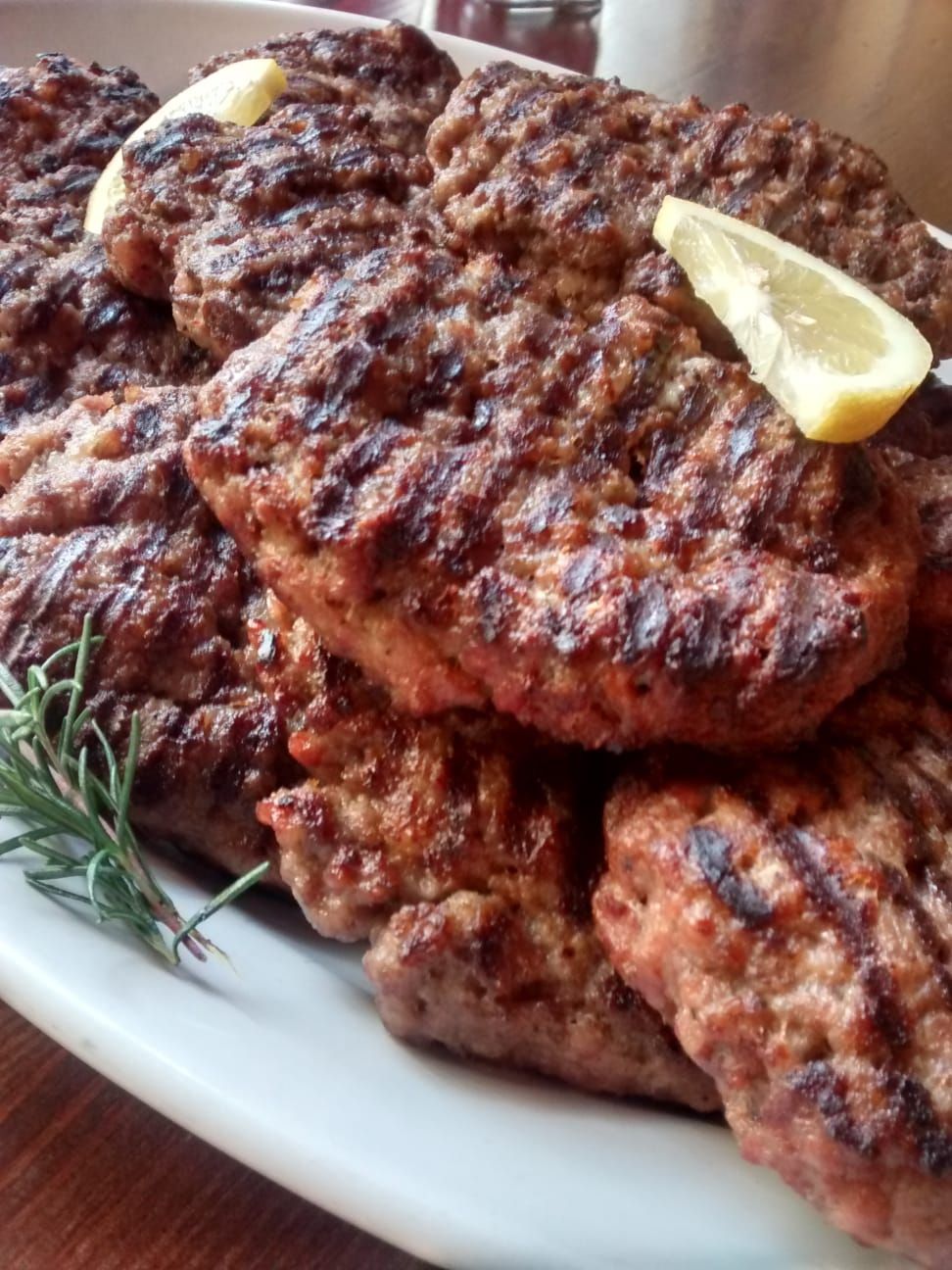Polpette di carne grigliate su un piatto bianco con uno spicchio di limone e un rametto di rosmarino.