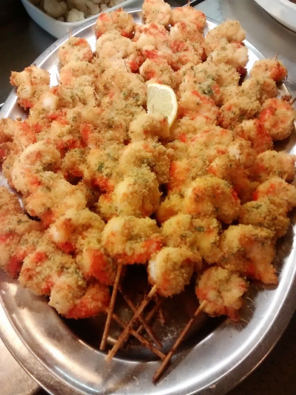 Vassoio di spiedini dorati fritti, conditi con spezie rosse e spicchi di limone.