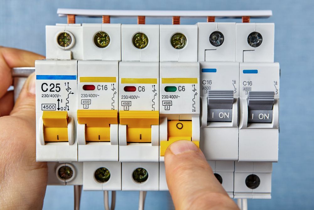 Hand turning a yellow switch on a row of circuit breakers in an electrical panel — Instant Spark Electrical in Glen Isla, QLD