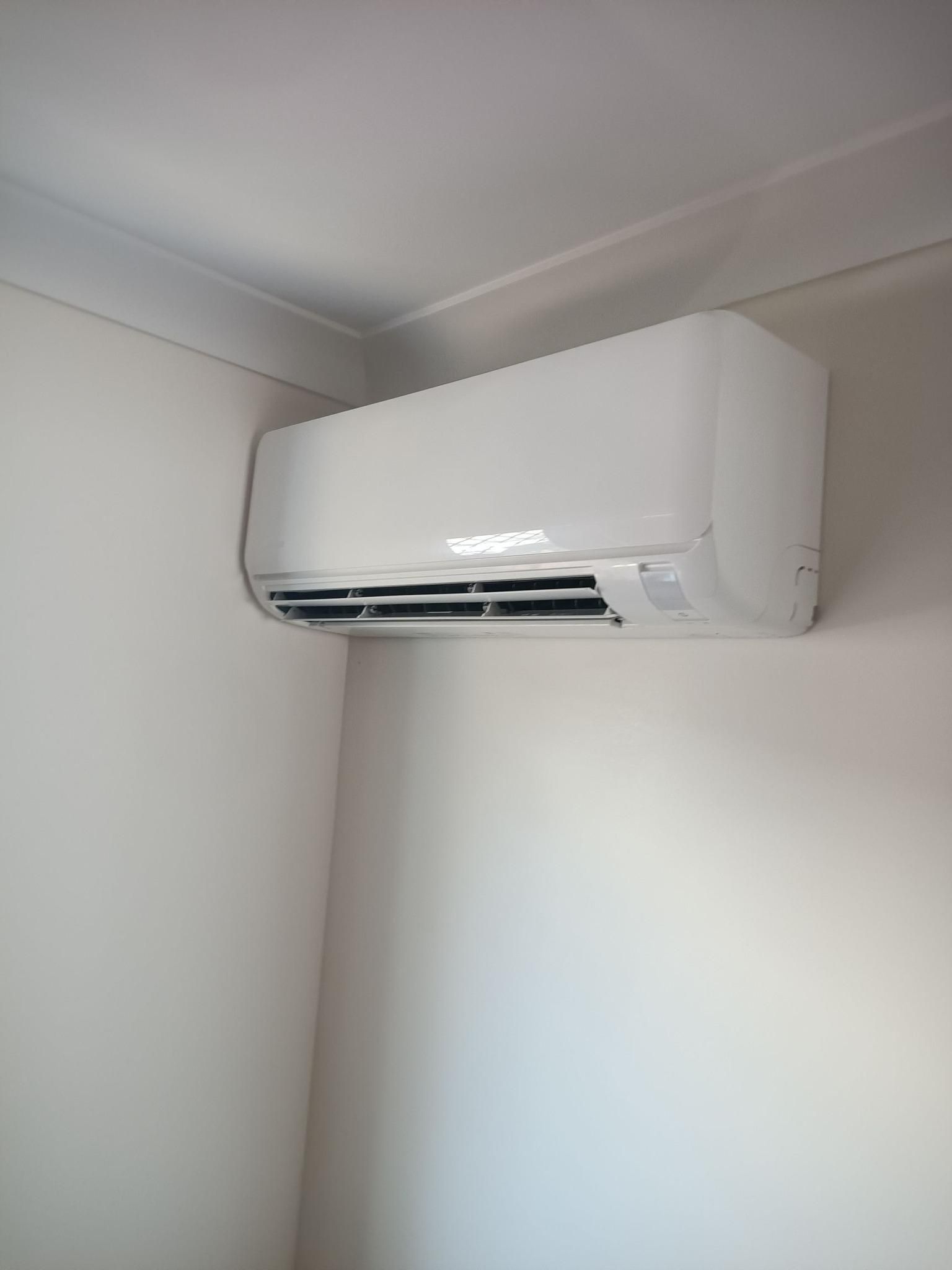 An Air Conditioner is Hanging on a White Wall in a Room — Instant Spark Electrical in Glen Isla, QLD