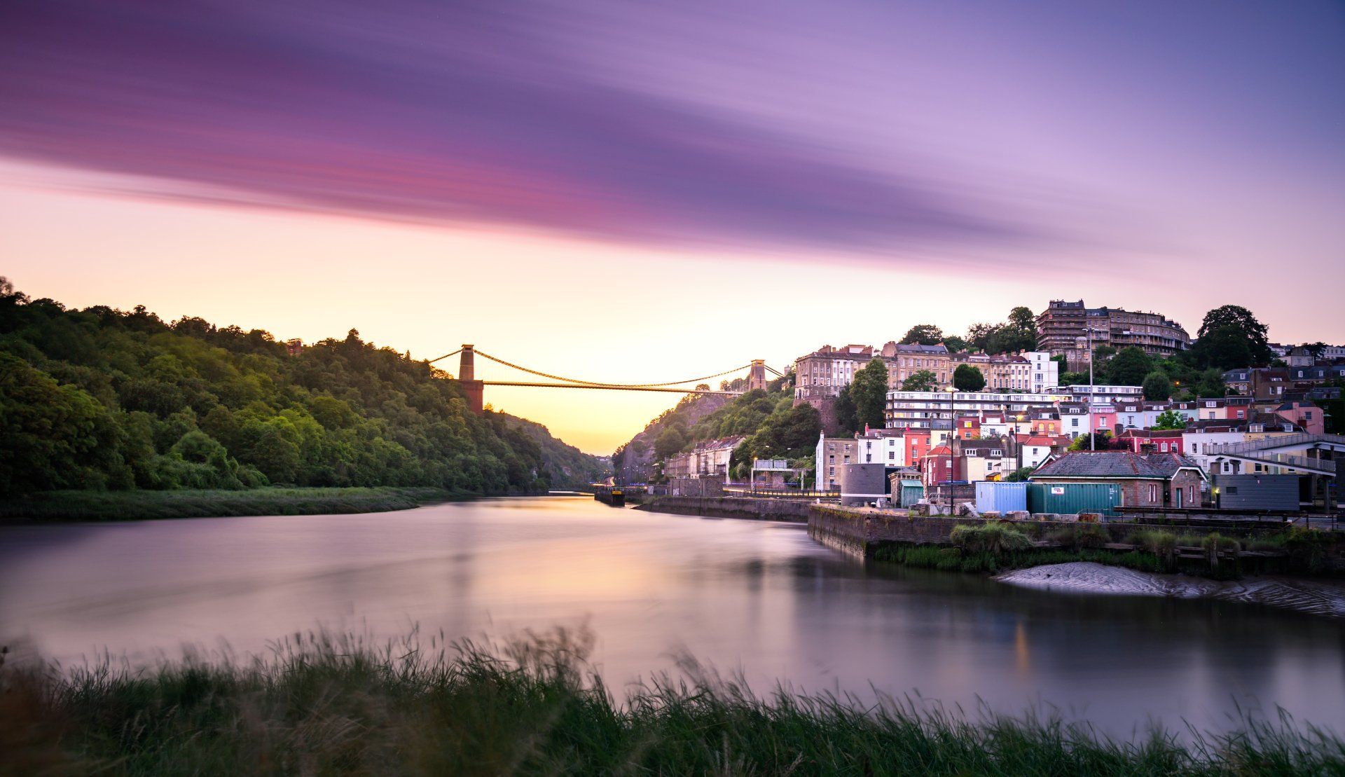 A bridge over a river with a city in the background at sunset.