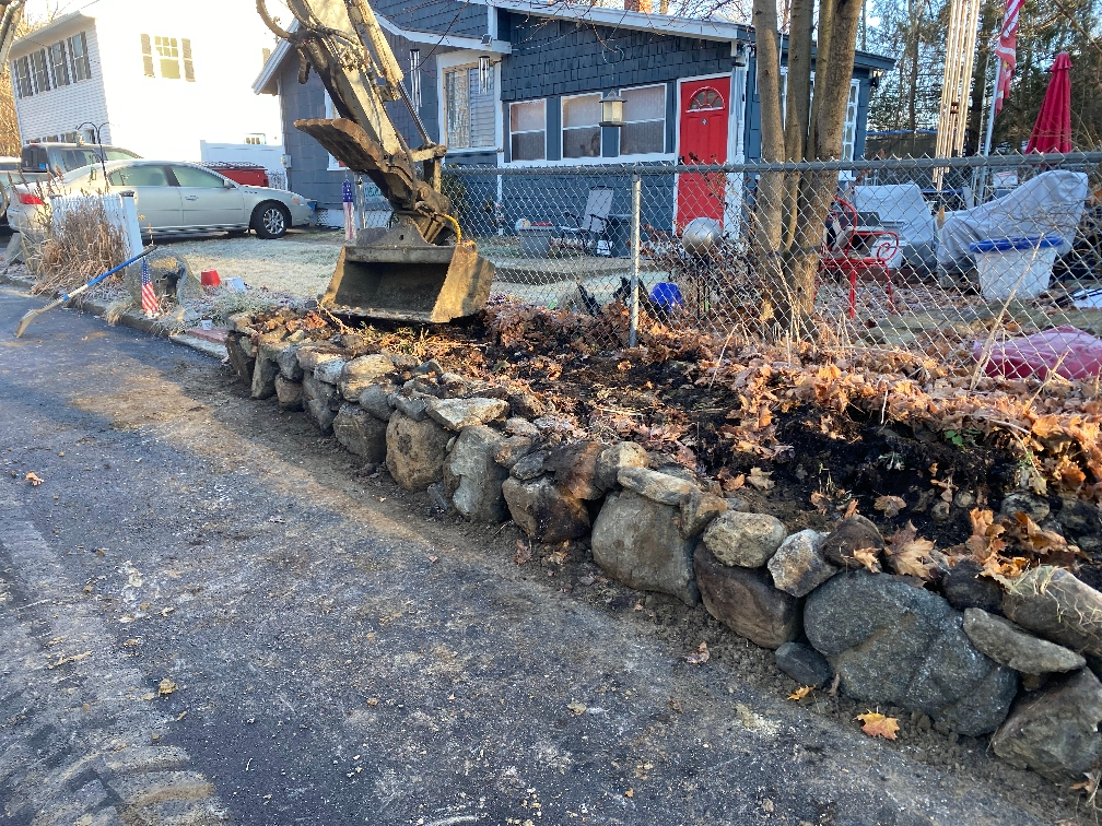 A bulldozer is digging a hole in the ground next to a stone wall.
