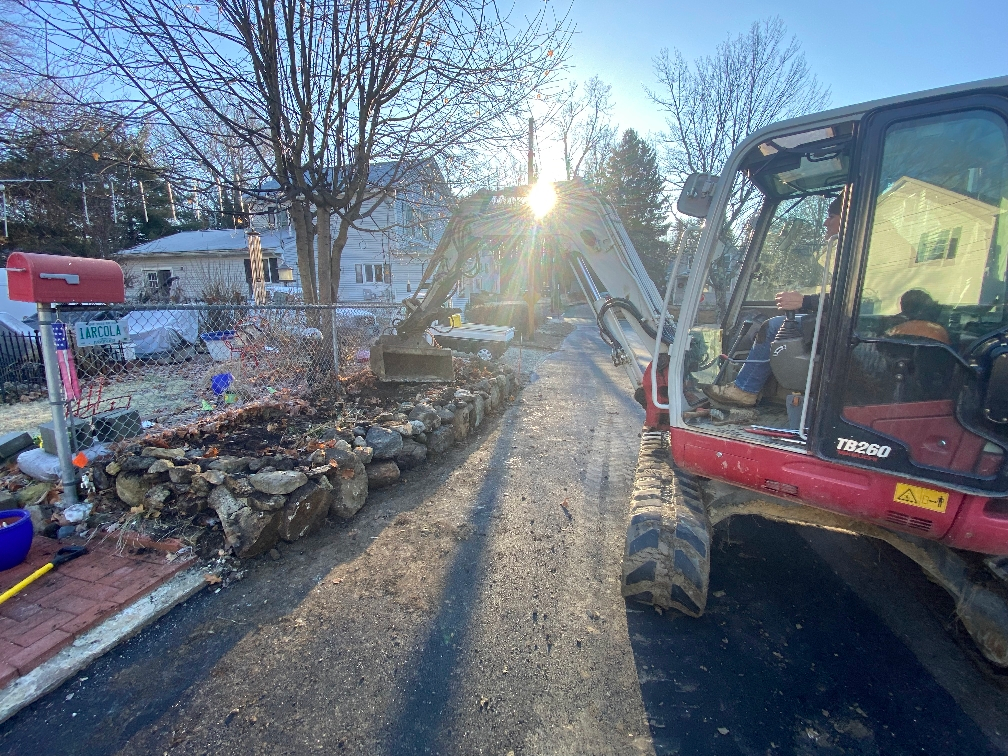 A red and white excavator is parked on the side of a road next to a pile of rocks.