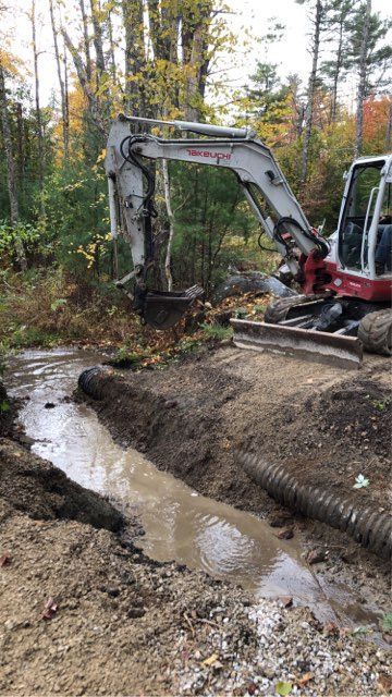 A white and red excavator is digging a stream in the woods.