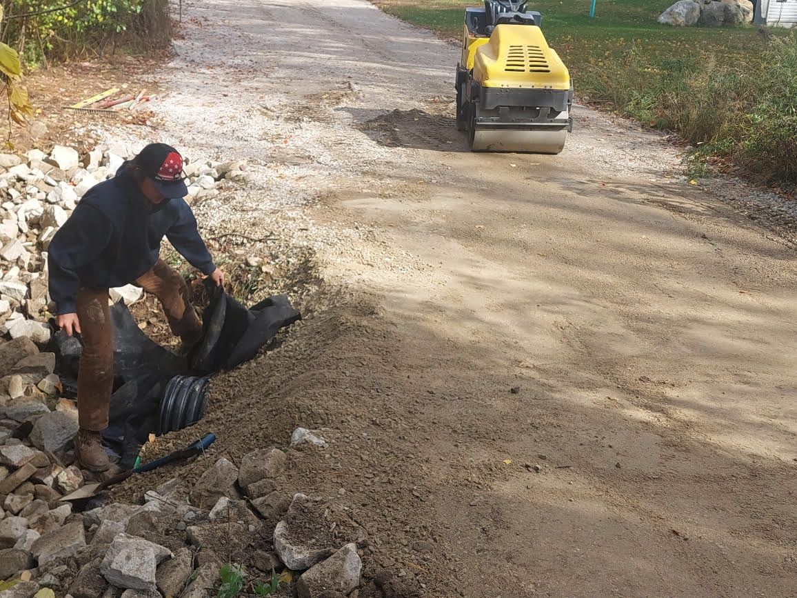 A man is standing next to a yellow roller on a dirt road.