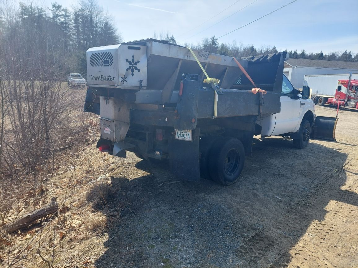 A white truck with a snow plow attached to it is parked in a dirt field.