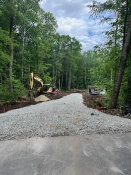 A yellow excavator is working on a gravel road in the woods.