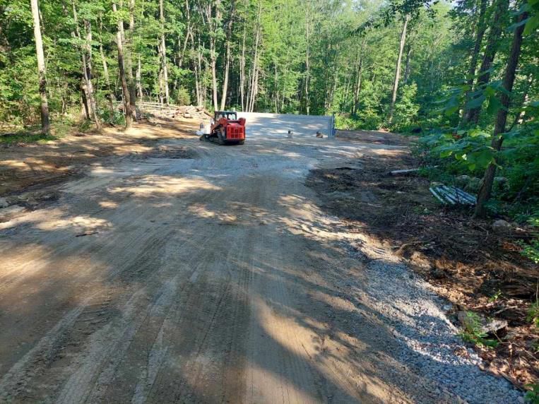 A red truck is driving down a dirt road in the woods.