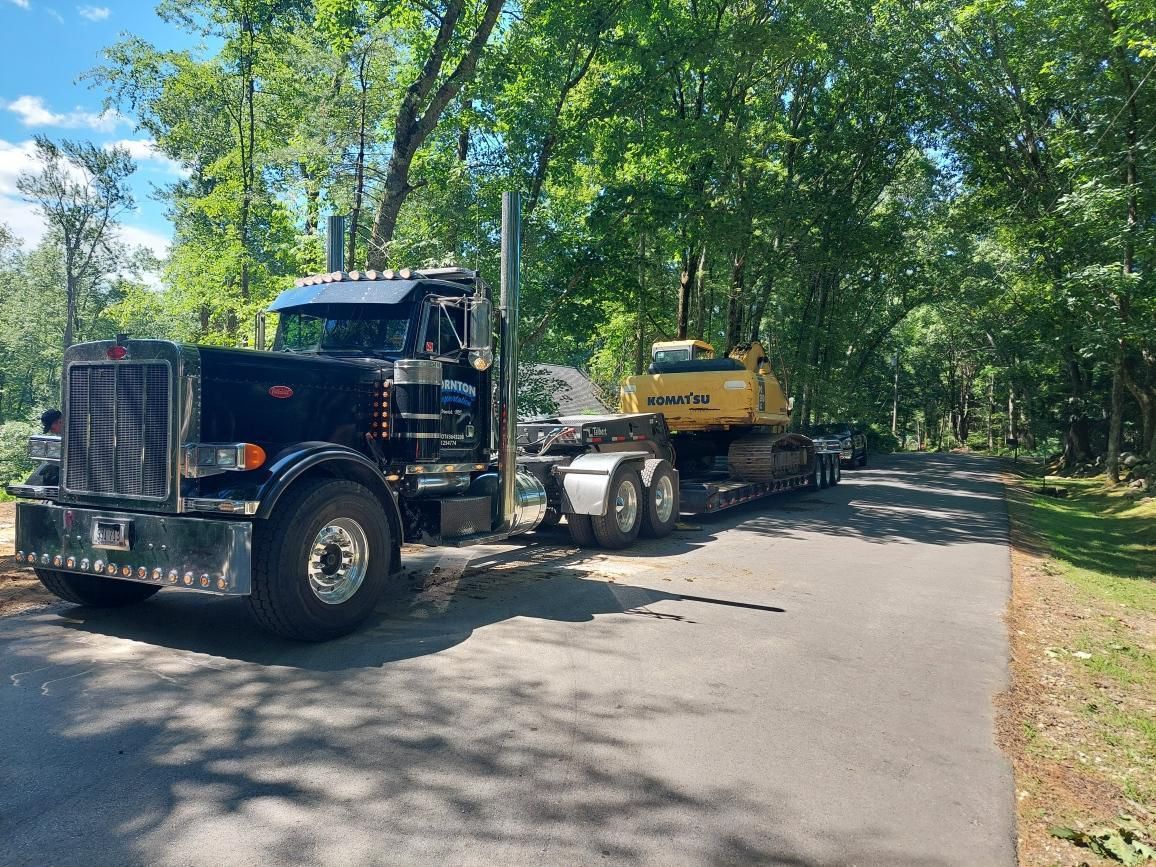 A black semi truck is carrying a yellow excavator down a road.