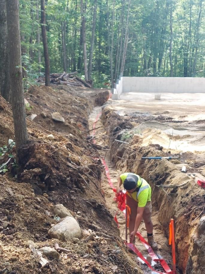 A man is working in a trench in the woods.