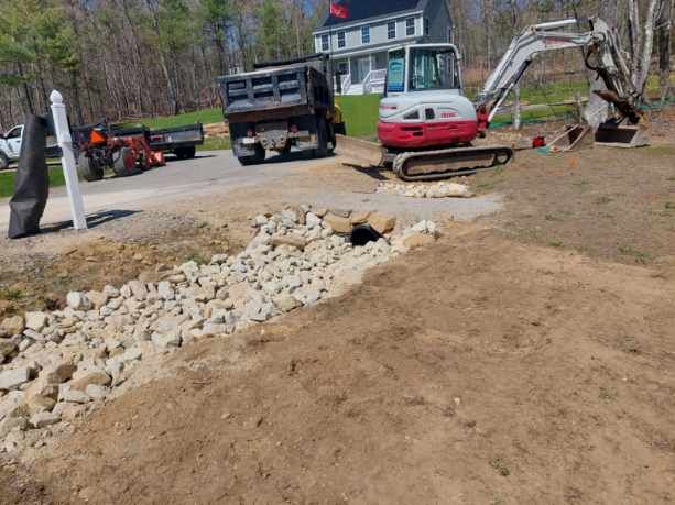 A dump truck is driving down a dirt road next to an excavator.