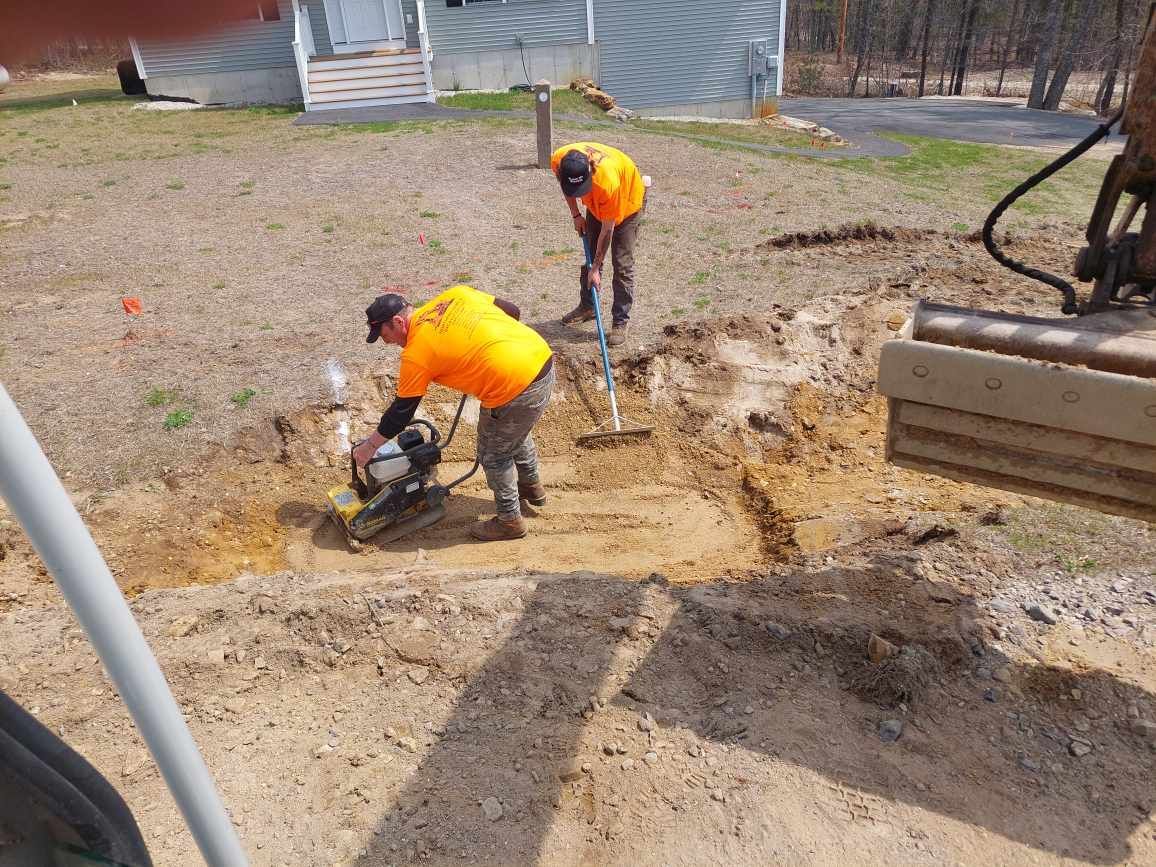 Two men are digging in the dirt in front of a house.