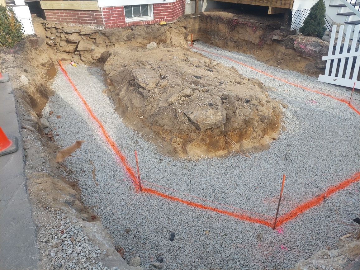 A large pile of dirt and gravel is being excavated in front of a house.