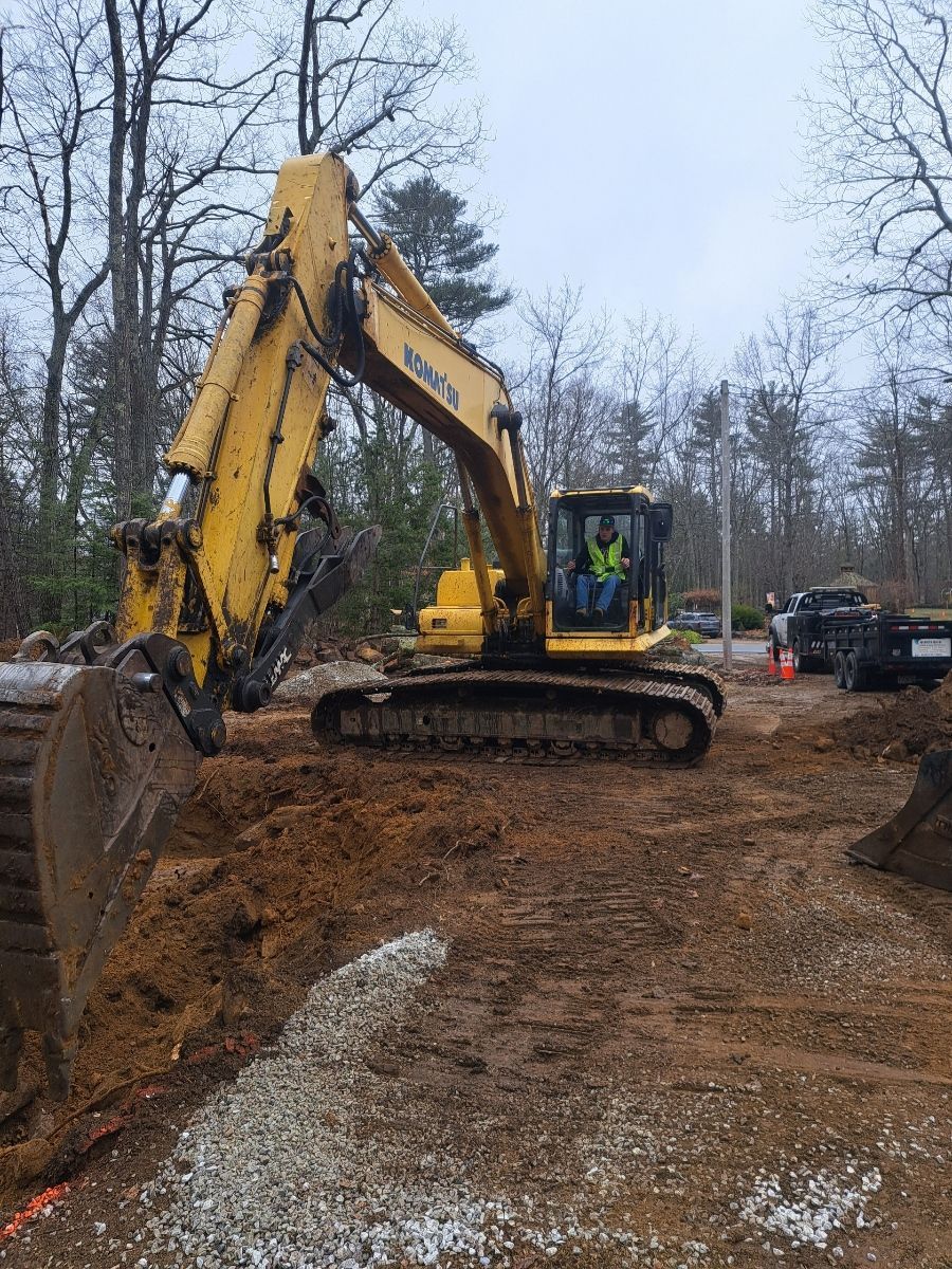 A man is driving a yellow excavator on a dirt road.