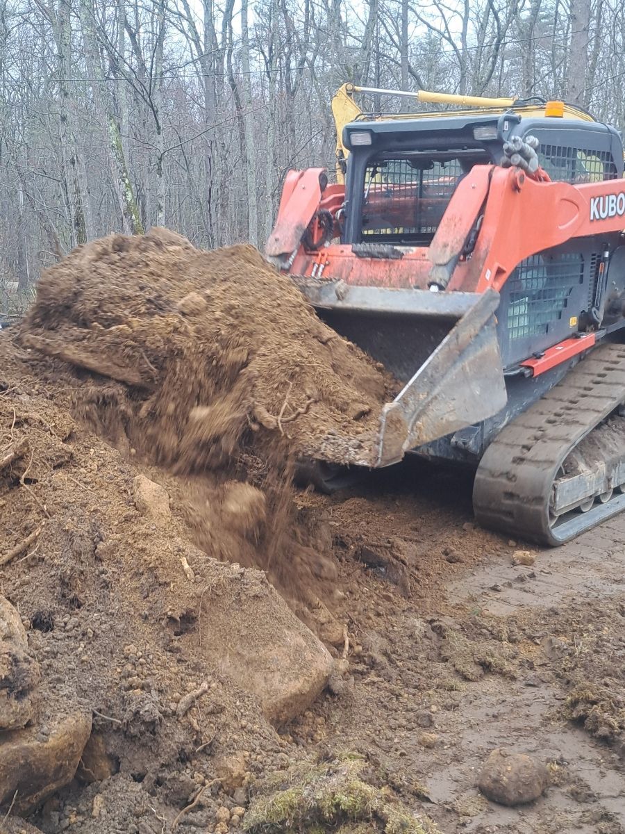 A bulldozer is moving a pile of dirt in the woods.