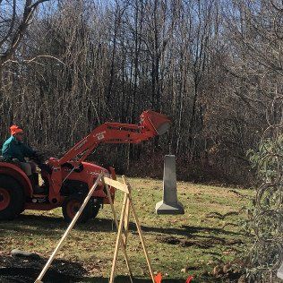 Worker Operating a Small Backhoe to Lift Concrete Site Markings