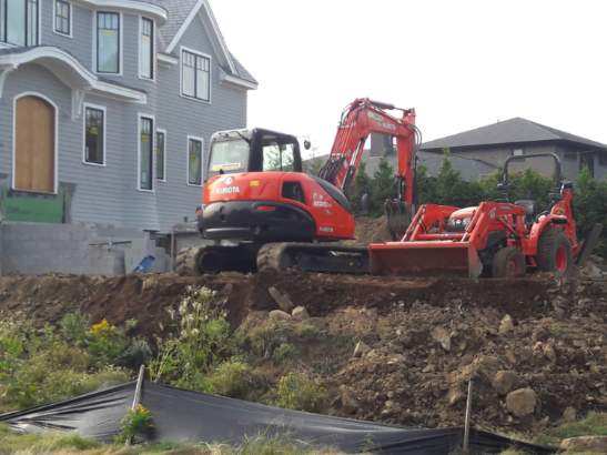 An excavator is digging a hole in front of a house.
