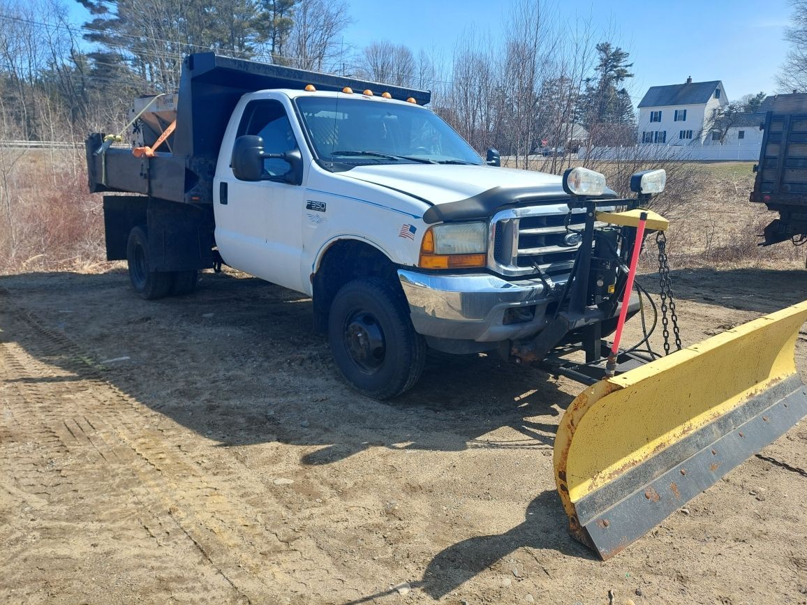 A dump truck with a snow plow attached to it is parked in a dirt field.