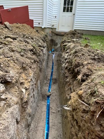 A blue pipe is being installed in a trench next to a house.