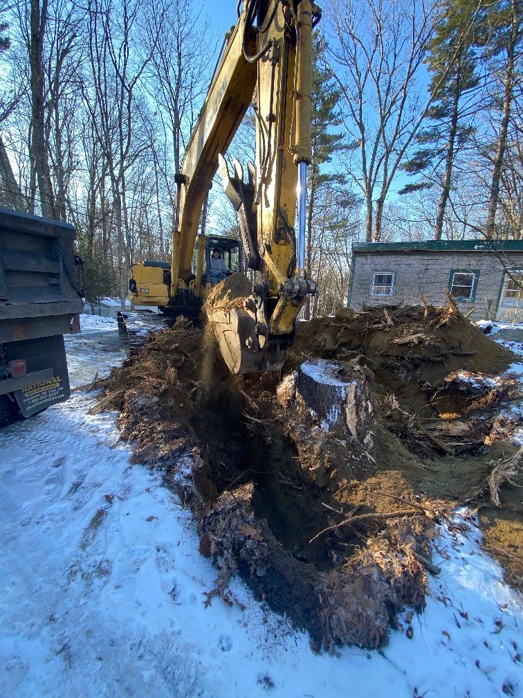A large excavator is digging a hole in the snow next to a dump truck.