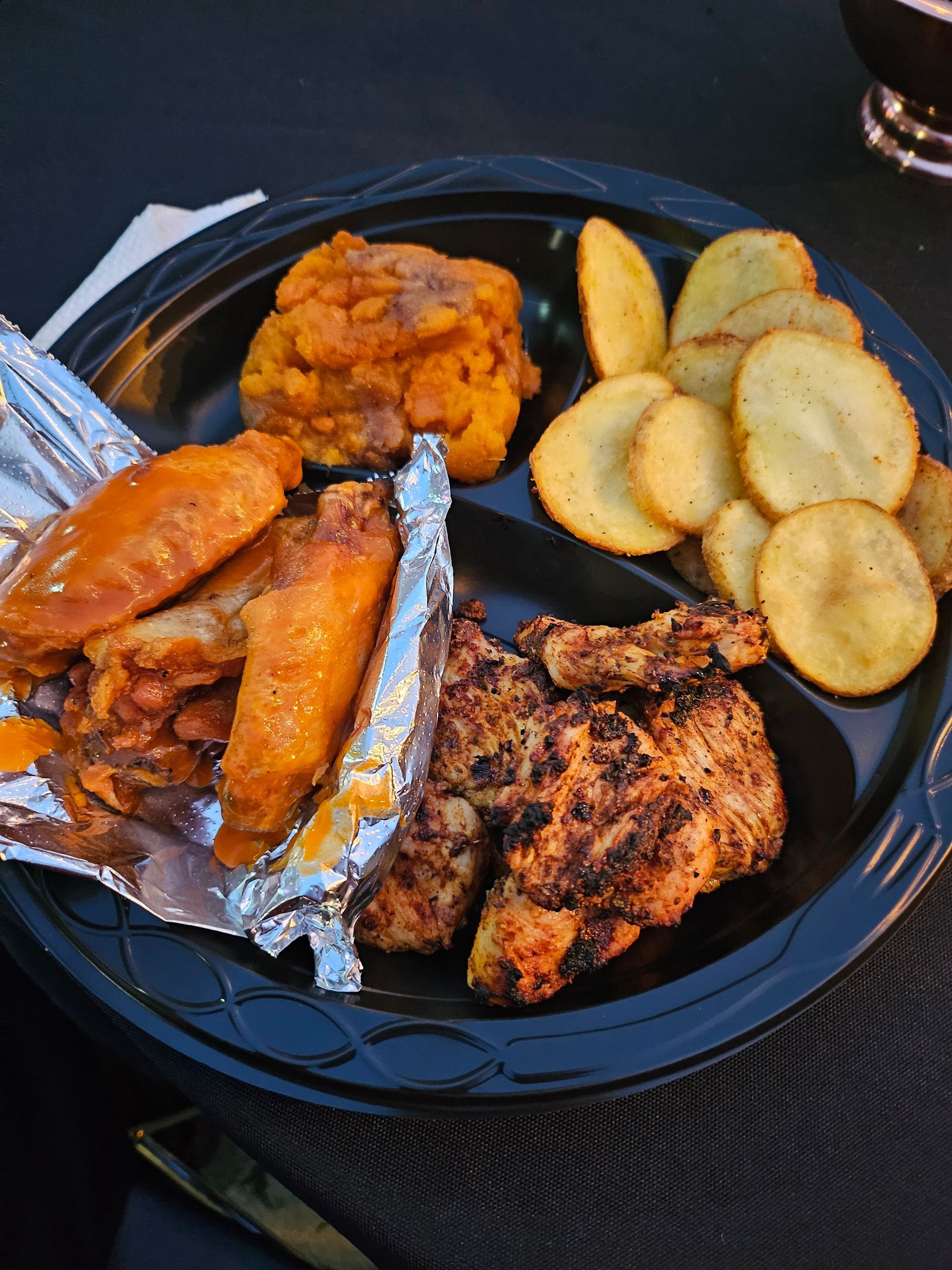 A plastic plate with chicken wings and potato chips on it