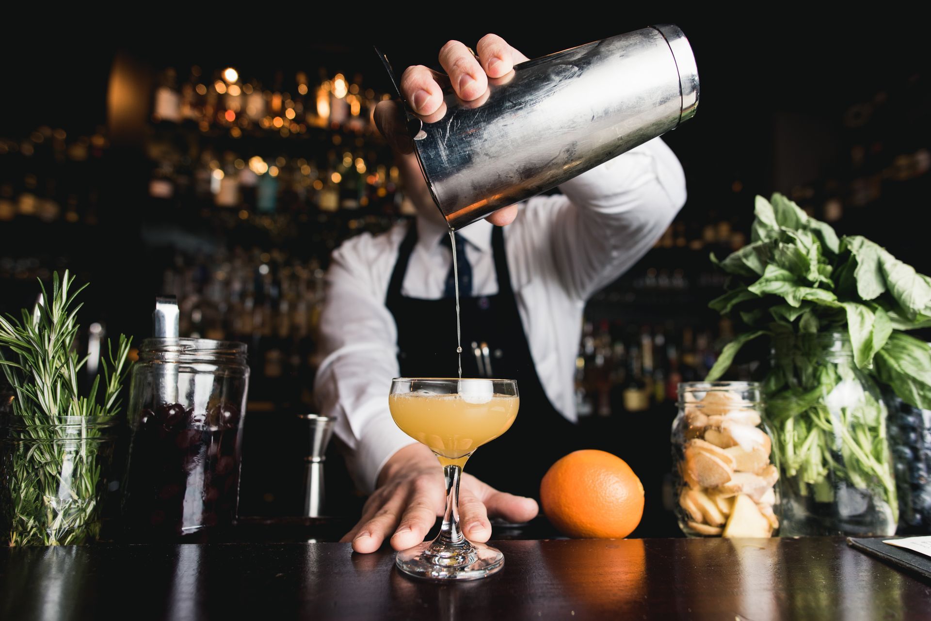 A bartender is pouring a drink from a shaker into a glass.