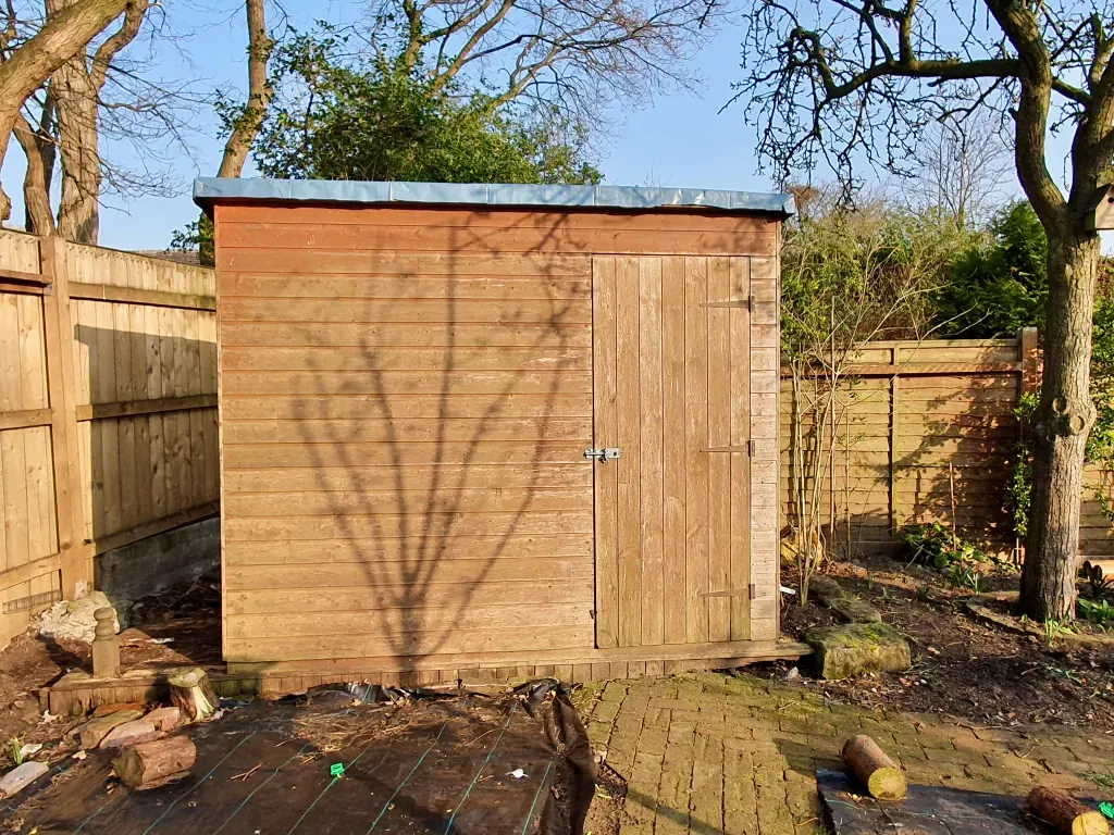 A wooden shed in a backyard with a fence and trees in the background.
