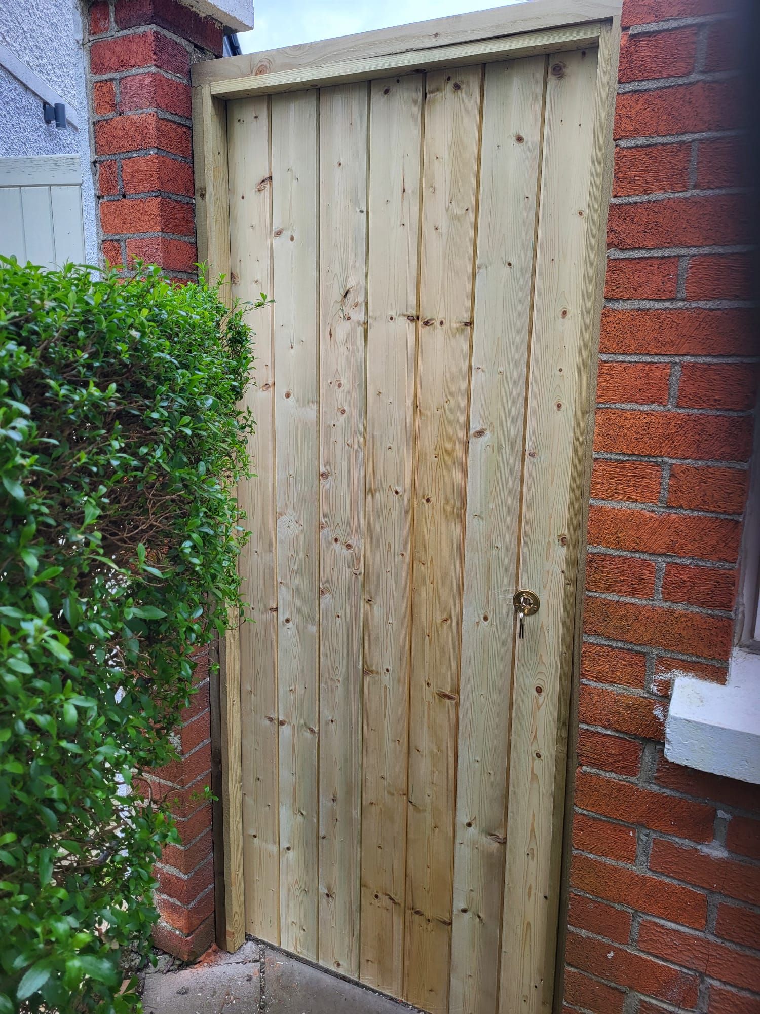 A wooden door is sitting on a brick wall next to a bush.