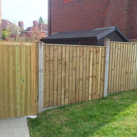A wooden fence with a gate in front of a brick building.