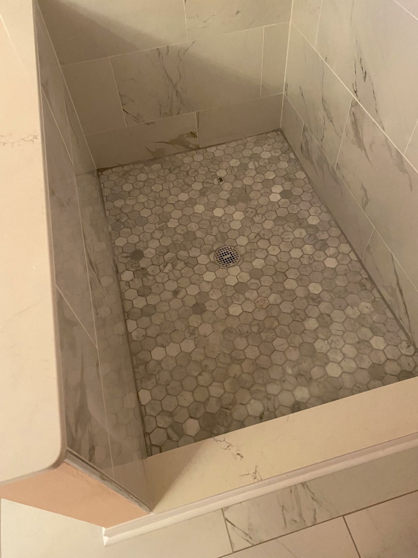 Shower with white and gray stone tile.  The floor is covered in small, gray, pebble-like tiles.