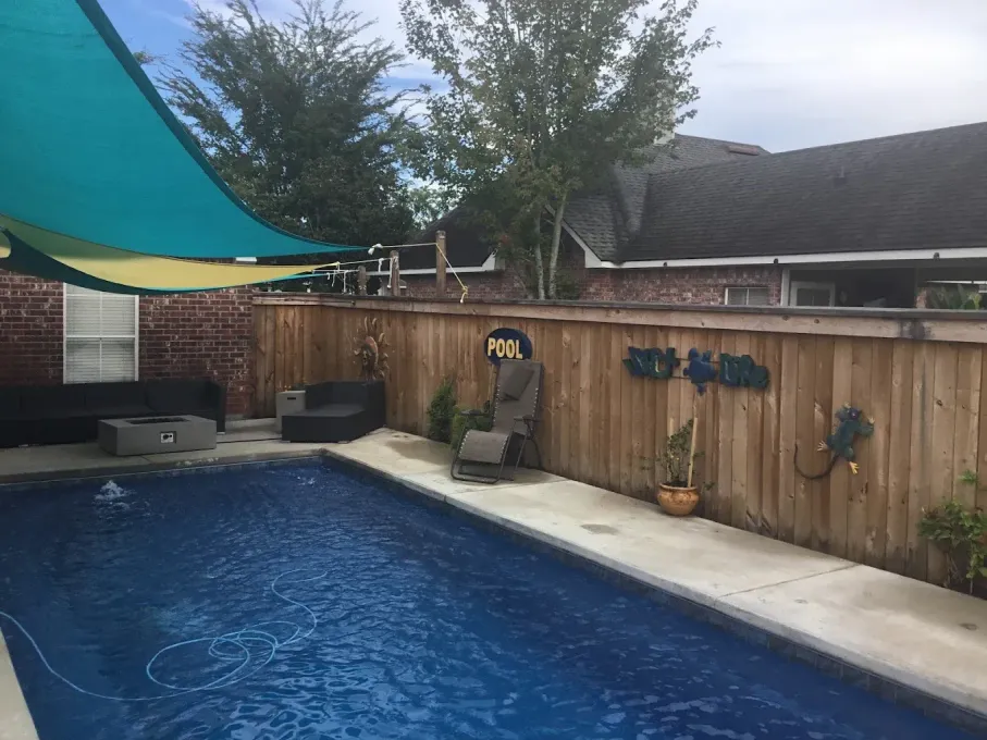 A large swimming pool is surrounded by a wooden fence and chairs.
