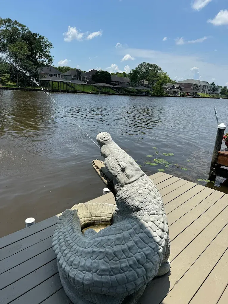 A statue of a crocodile is sitting on a dock next to a lake.