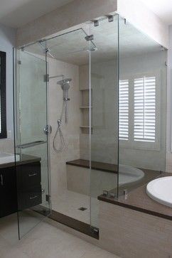Glass shower enclosure in a modern bathroom with a bench and window.