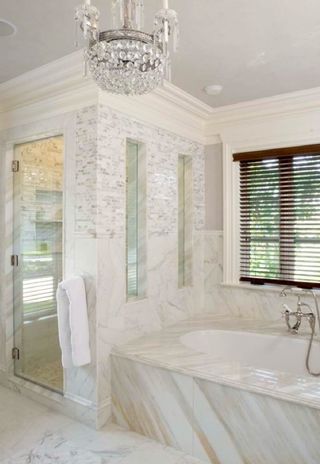 Elegant marble bathroom with a glass shower, tub, and a chandelier.