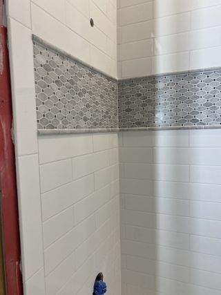 White tiled shower with a decorative gray mosaic band.
