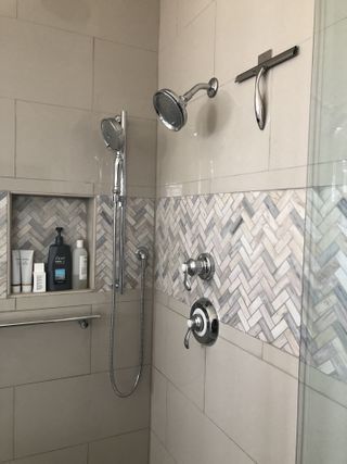 Modern shower with gray and white tile, handheld and fixed showerheads, and built-in shelf.