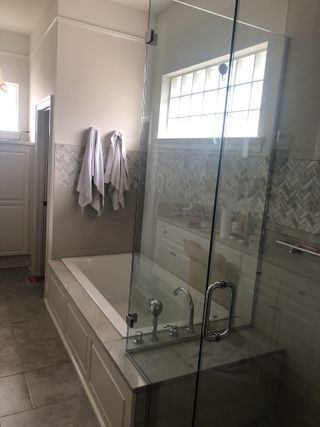Bathroom with a tub and glass shower, light-colored tile and cabinetry, towels hanging, a window above.