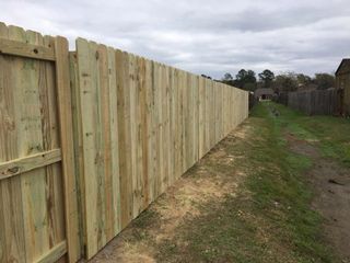 Wooden privacy fence stretches along a grassy path under a cloudy sky.