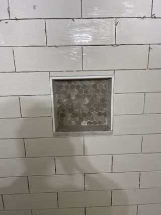 White tiled shower wall with a recessed niche containing grey hexagon tiles.