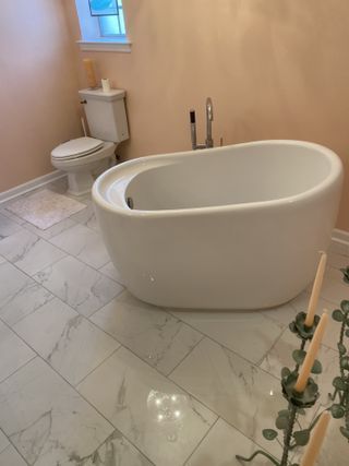 White oval bathtub in bathroom with peach walls and marble floors. Toilet is visible behind.