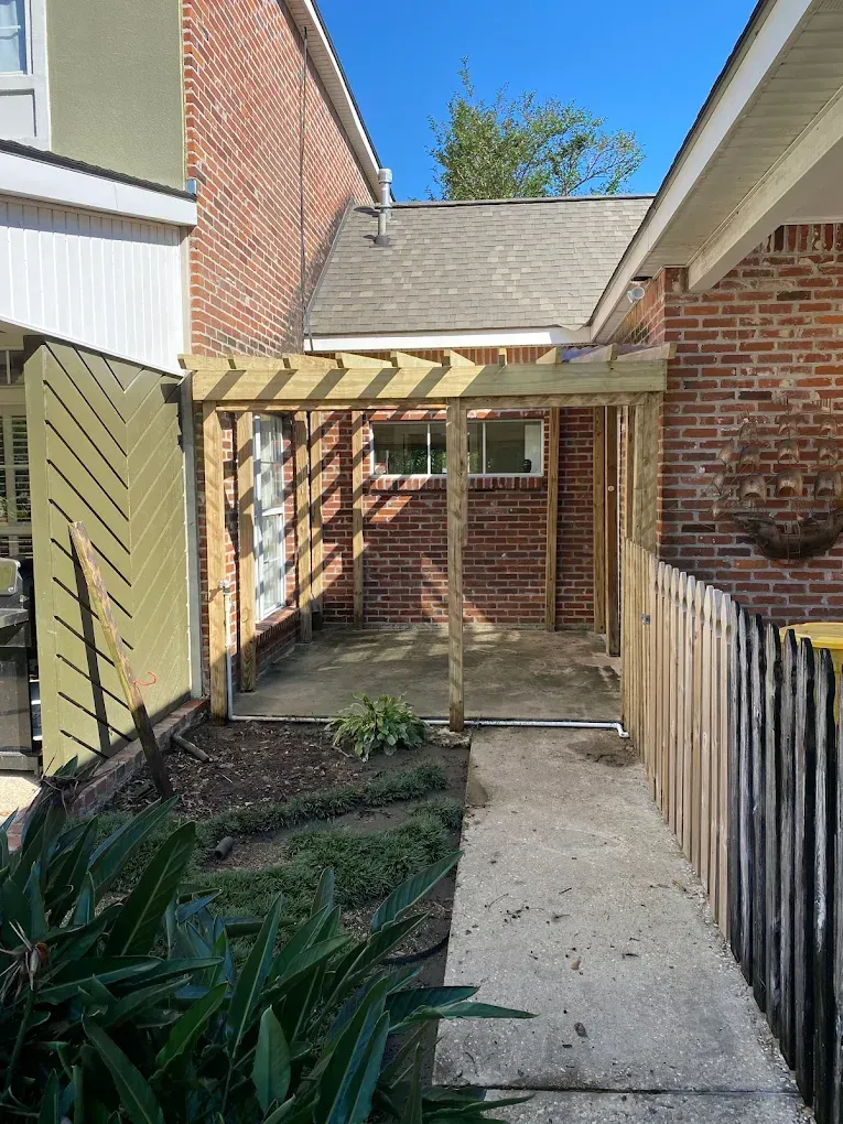 A wooden pergola is being built in the backyard of a brick house.
