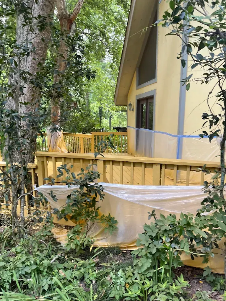 A wooden deck with a hammock on it in front of a house in the woods.