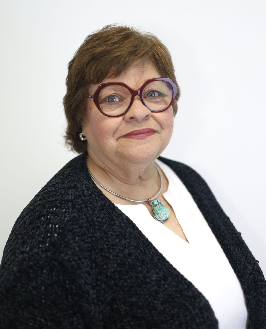 A woman wearing glasses and a necklace is smiling for the camera