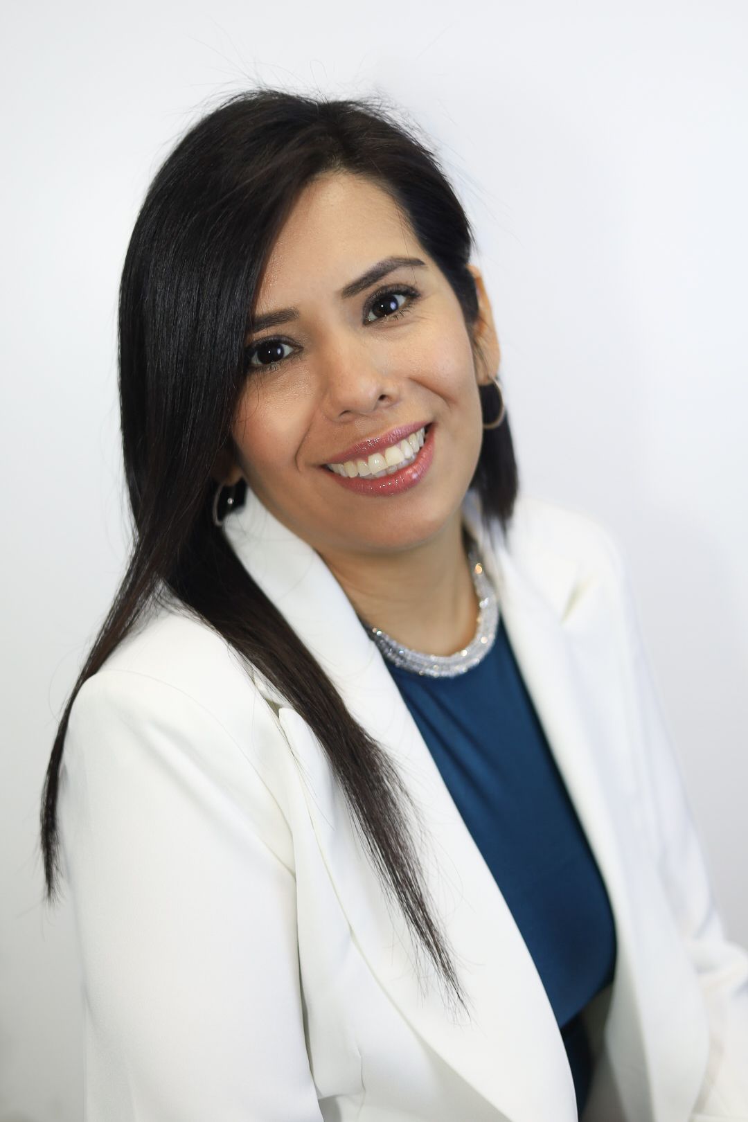 A woman wearing a white jacket and a blue shirt is smiling for the camera.