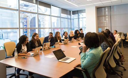 A group of people are sitting around a long conference table with laptops.