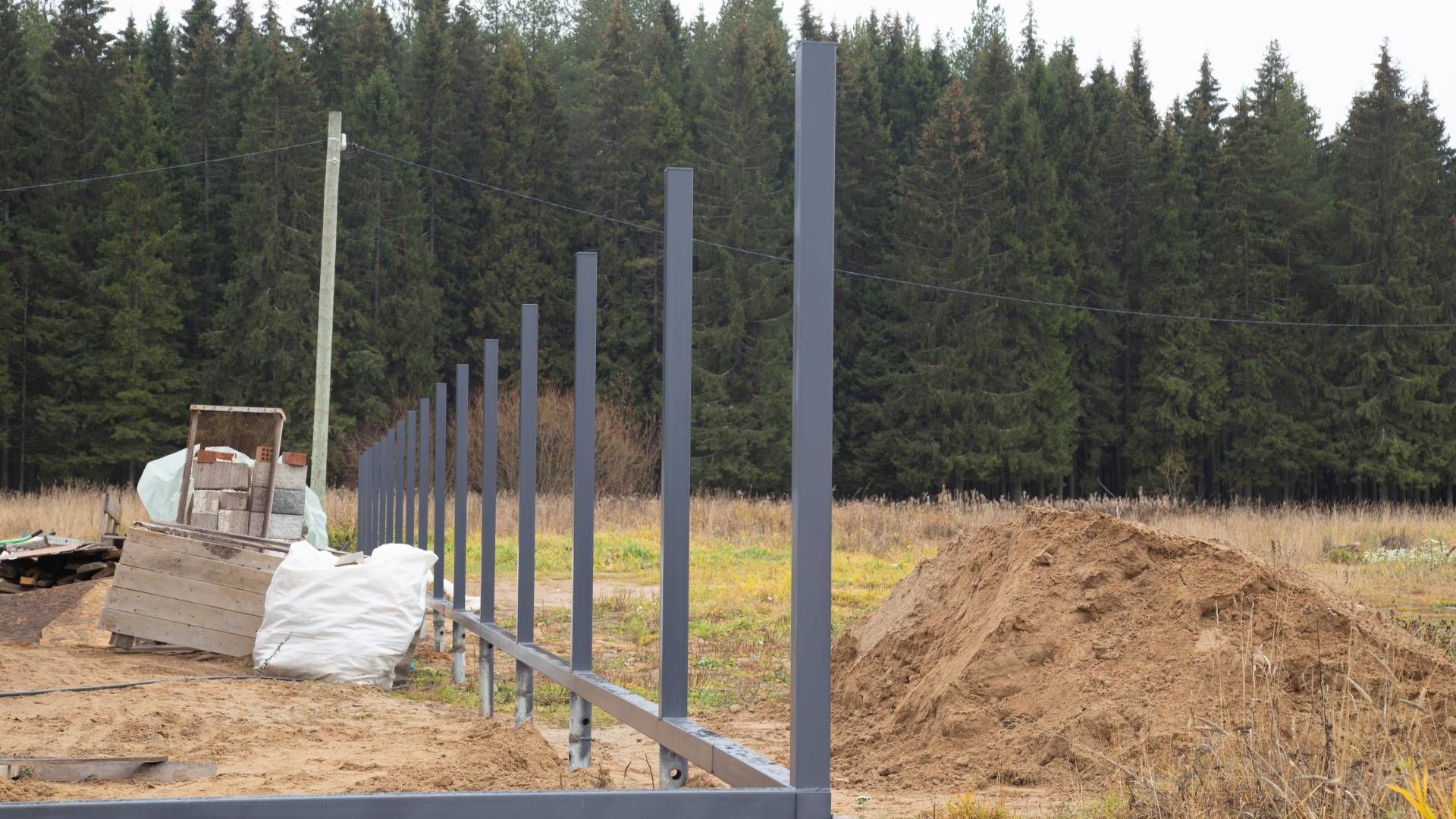 Fence construction in progress, metal posts installed, with a forest background.