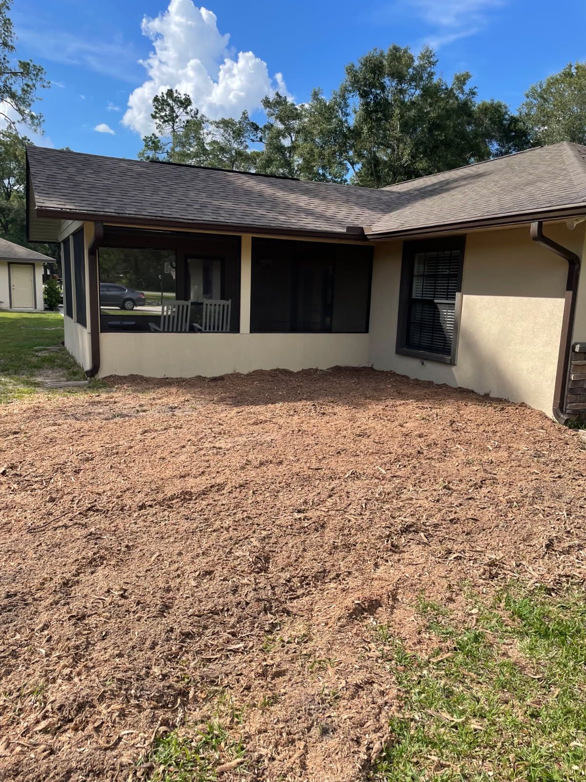 A house exterior with a screened porch and mulch in the yard under a blue sky.